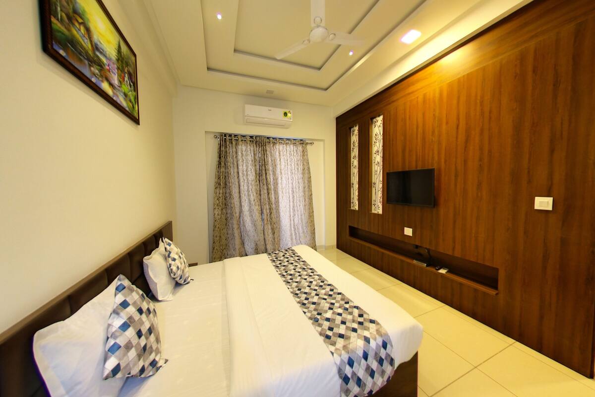 A hotel room with a bed, a television, an air conditioning unit, and a wooden wardrobe.