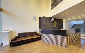 A reception area with a marble reception desk, a brown leather sofa, and a staircase in the background. - Anantam Resort (Mendarda)