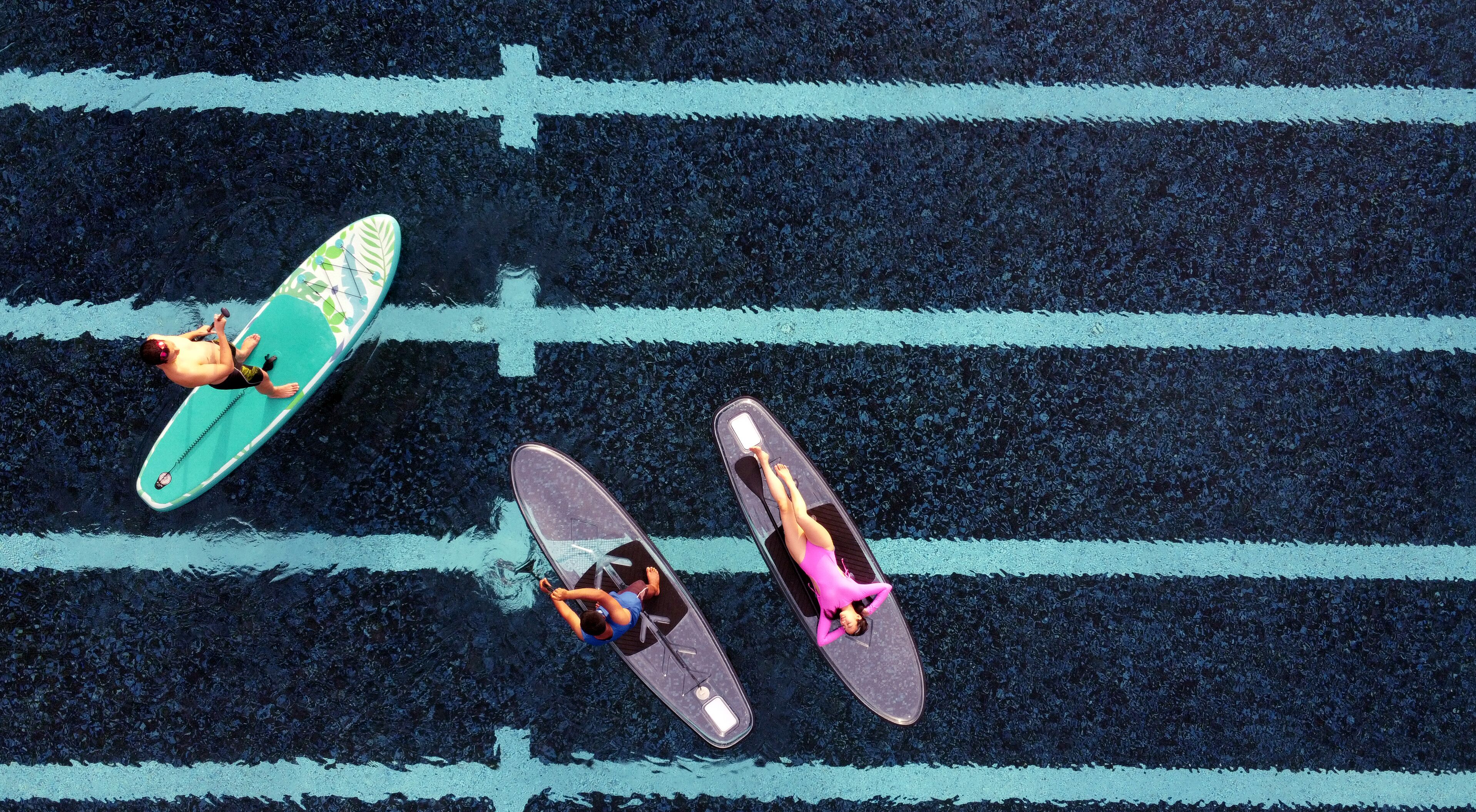 An aerial view of a beach with three people on surfboards.