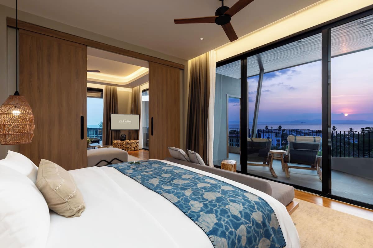 A modern hotel room with a large bed, a ceiling fan, a TV, and a balcony with a city view.