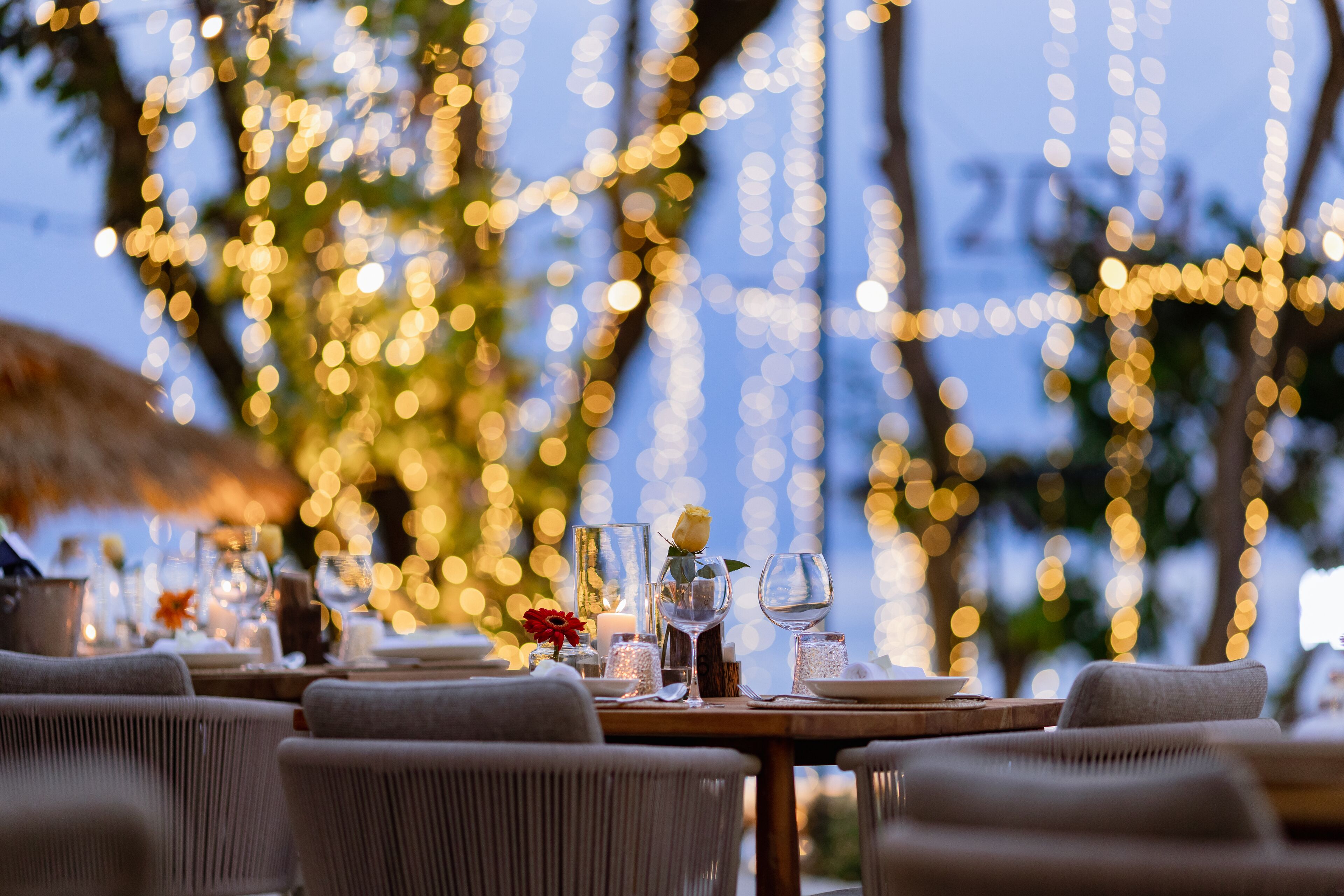 Un área de comedor al aire libre con mesas dispuestas para dos, con velas y cristalería.
