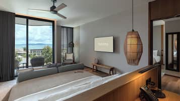 Een moderne hotelkamer met een groot bed, een bureau, een stoel, een staande lamp en uitzicht op zee.