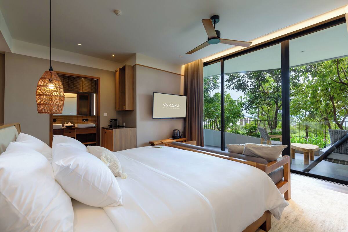 A modern bedroom with a large bed, a ceiling fan, and a view of the outdoors.