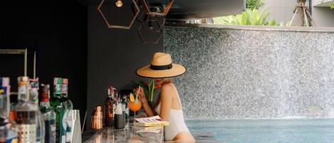 A person in a white swimsuit at a poolside bar with various bottles and a magazine.