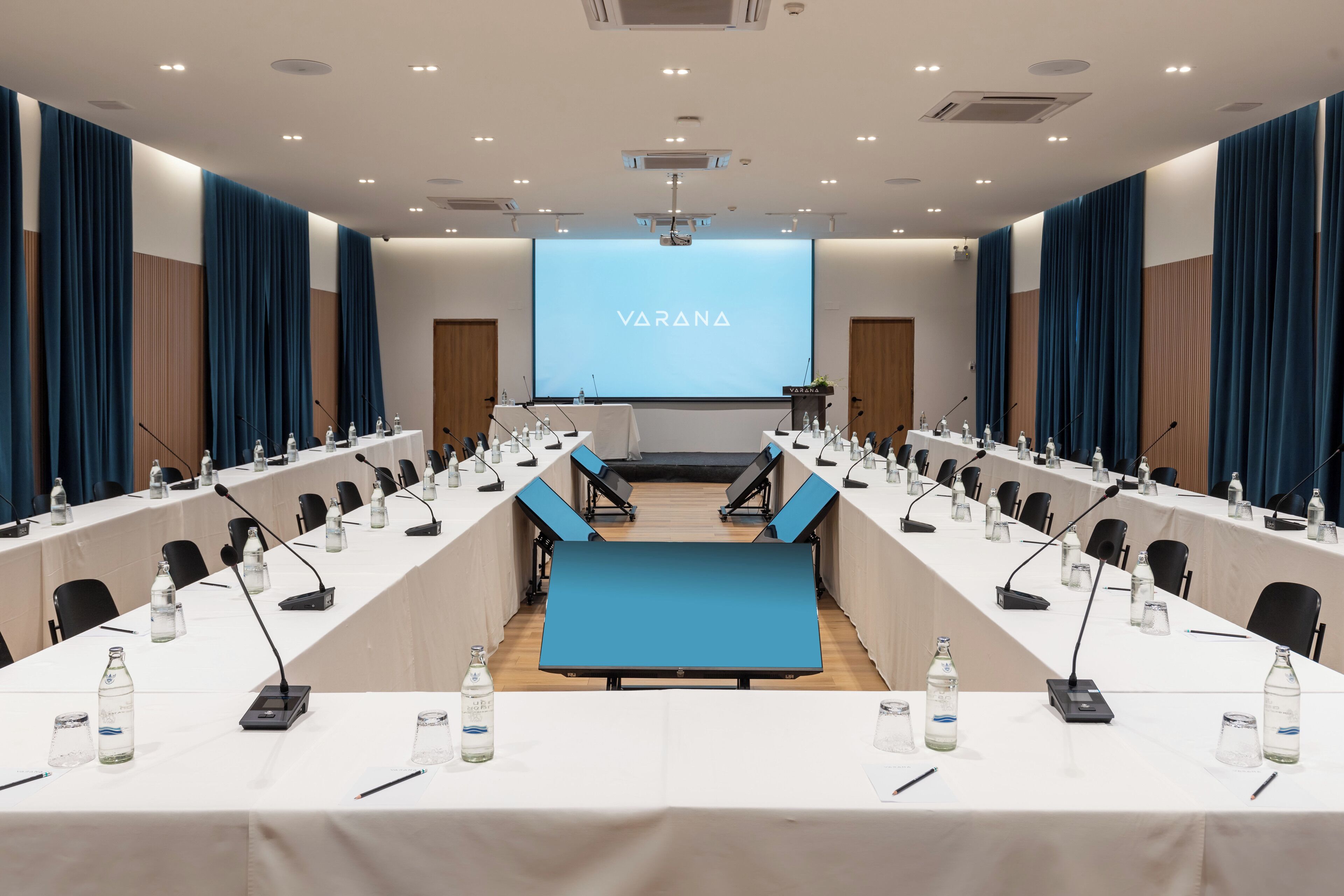 Une salle de conférence avec une longue table, des microphones et un écran affichant le mot « VARANA ».