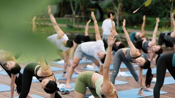 Um grupo de pessoas praticando yoga em tapetes azuis sobre um deck de madeira.