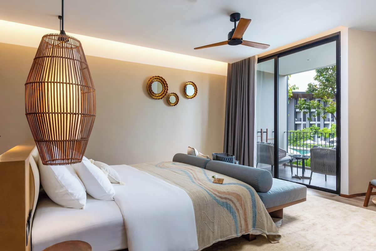 A modern bedroom with a bed, a sofa, a ceiling fan, and a view of an outdoor area with a pool.