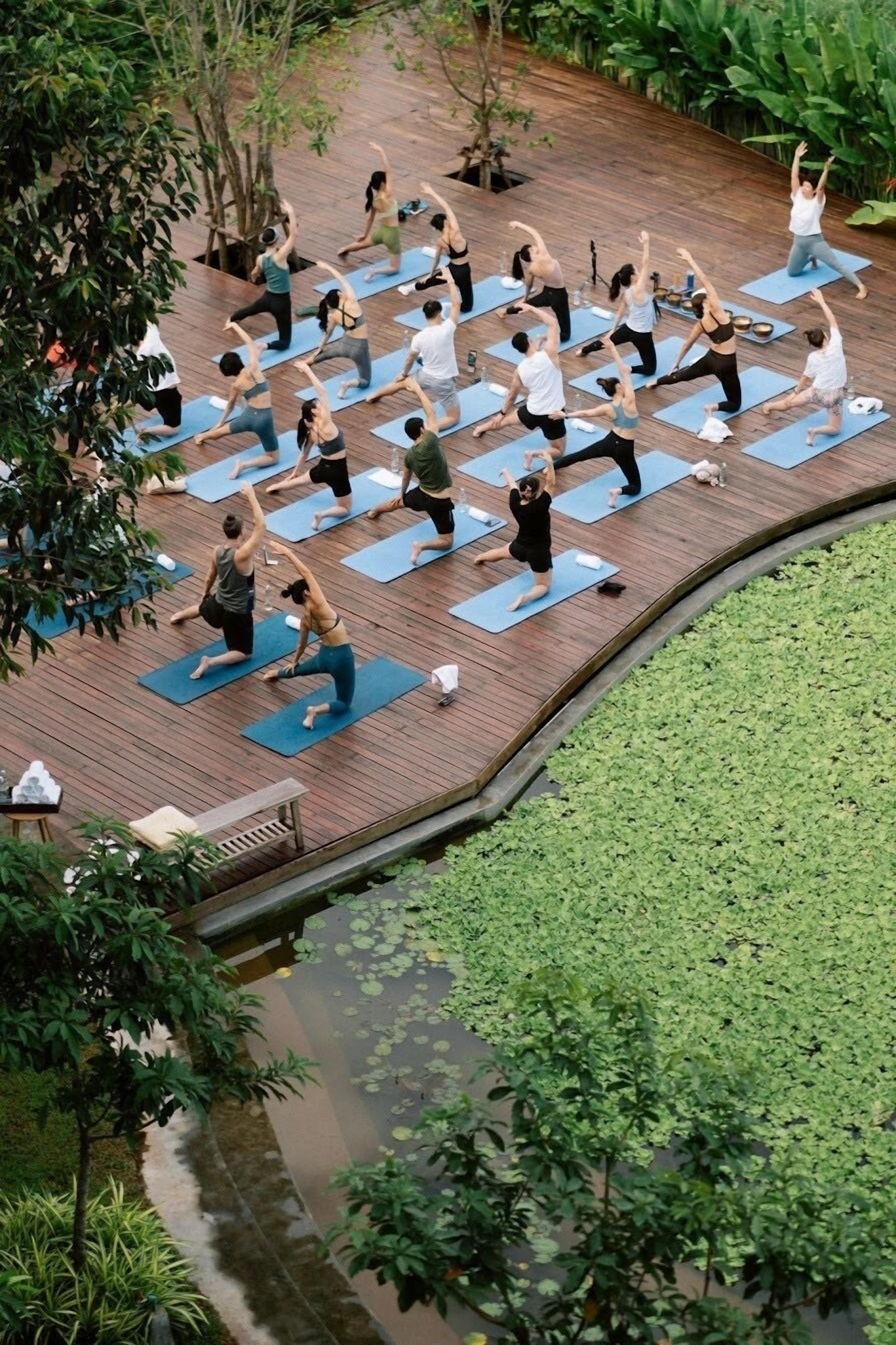 A group of people on yoga mats practicing in an outdoor setting with a wooden deck and a pond.