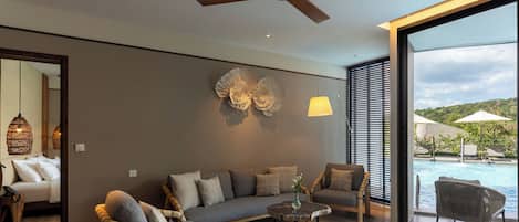 A modern living room with a sofa, chairs, a coffee table, and a large window overlooking a pool.