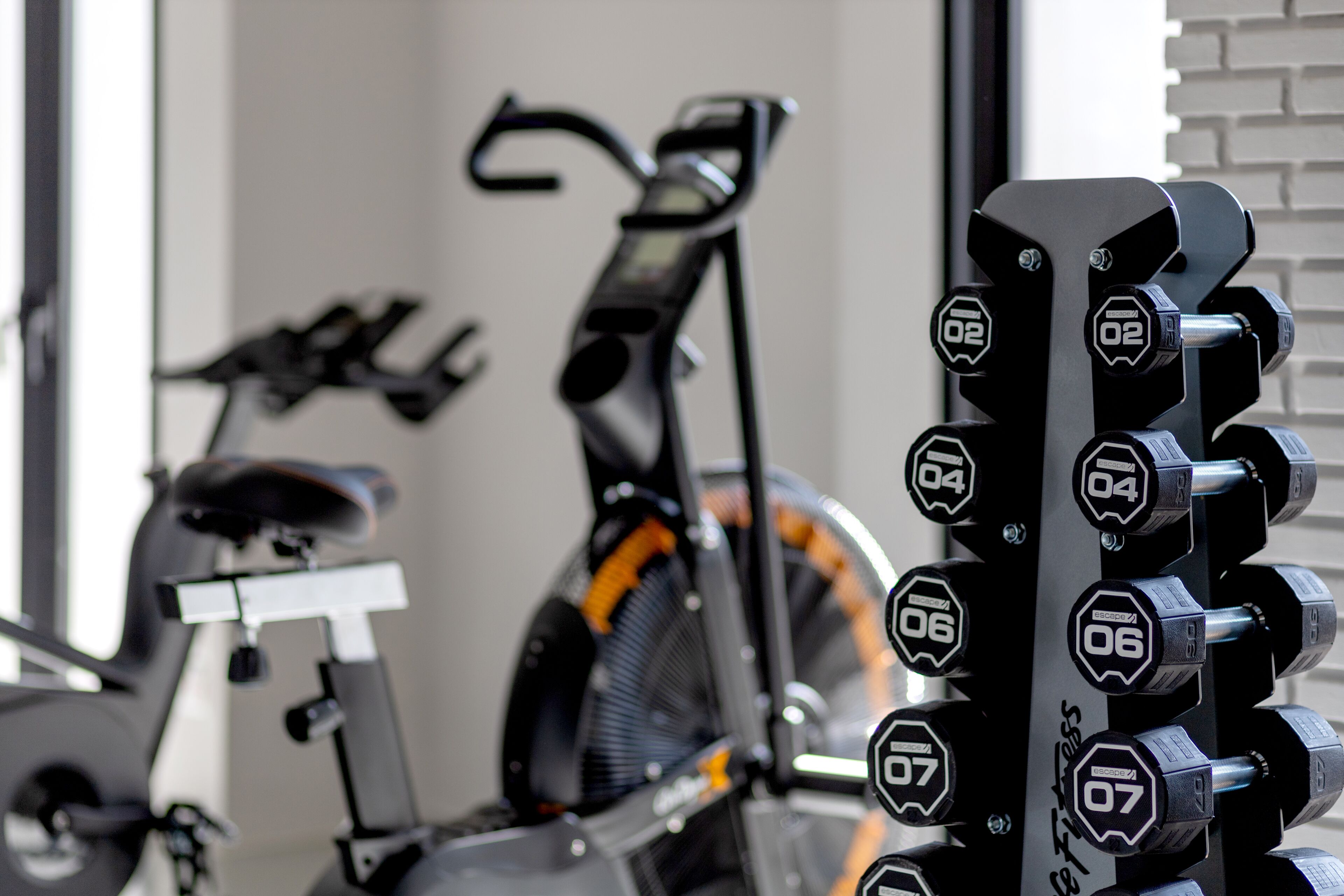 Een rij halters met gewichtsmarkeringen, een hometrainer en een loopband in een sportschool.