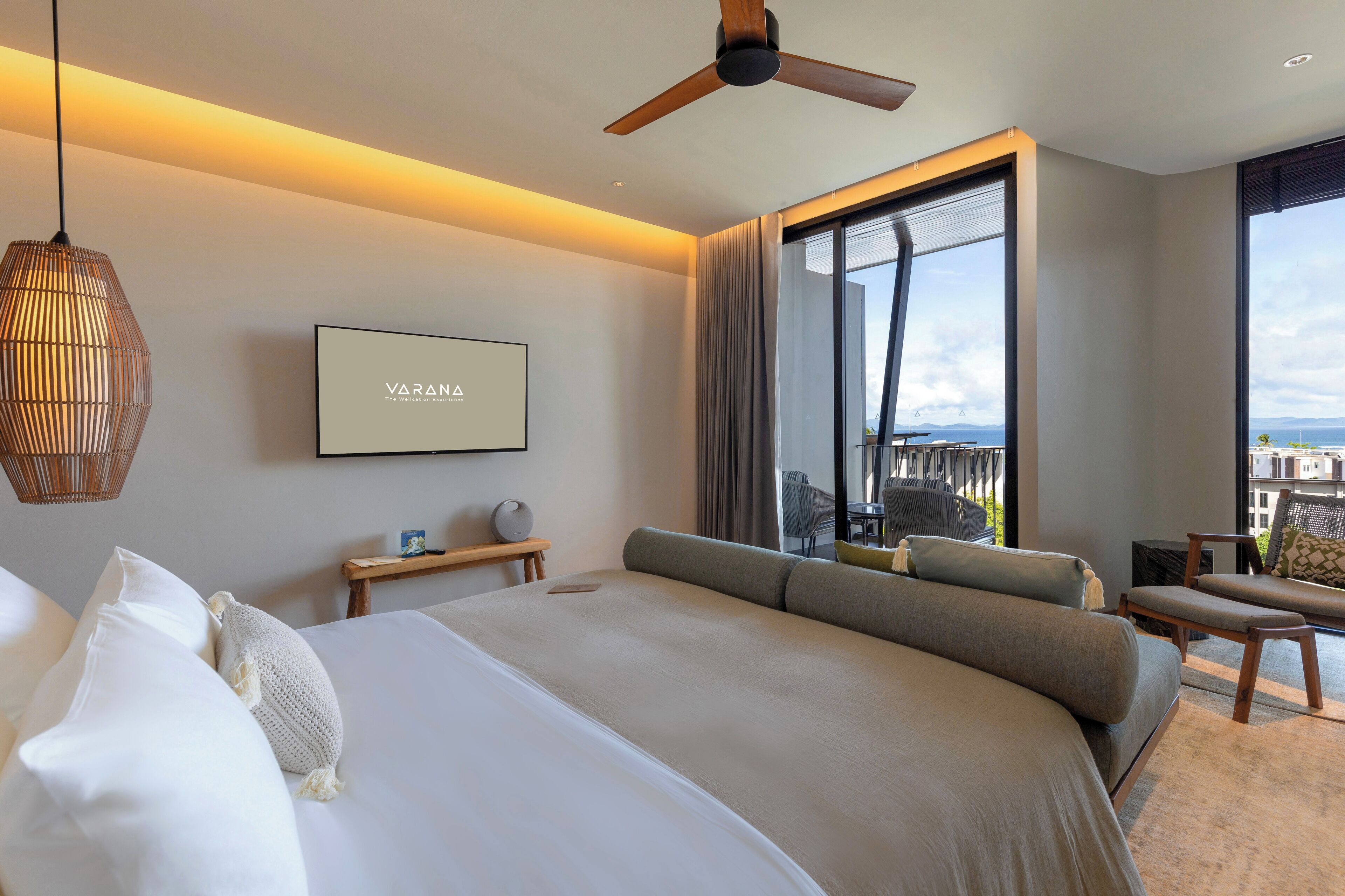 Una habitación de hotel moderna con una cama grande, ventilador de techo, televisor y balcón con vistas.
