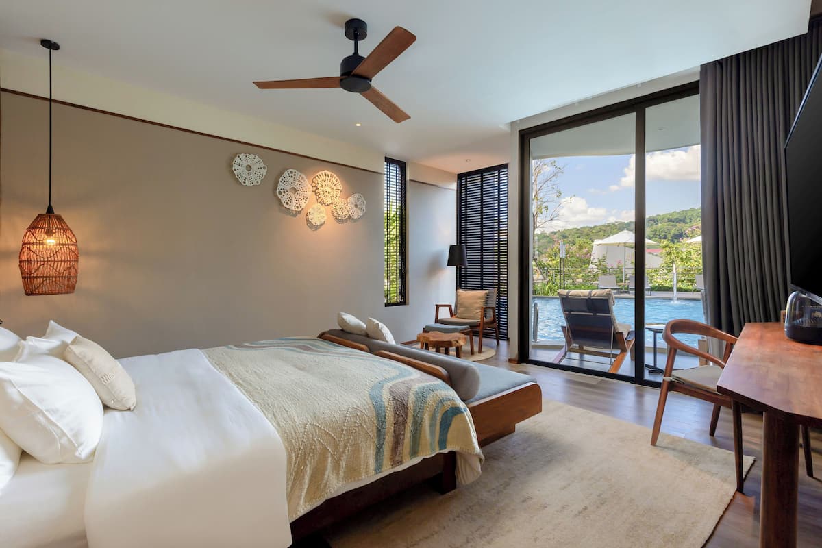 A modern bedroom with a large bed, a ceiling fan, and a view of a swimming pool.