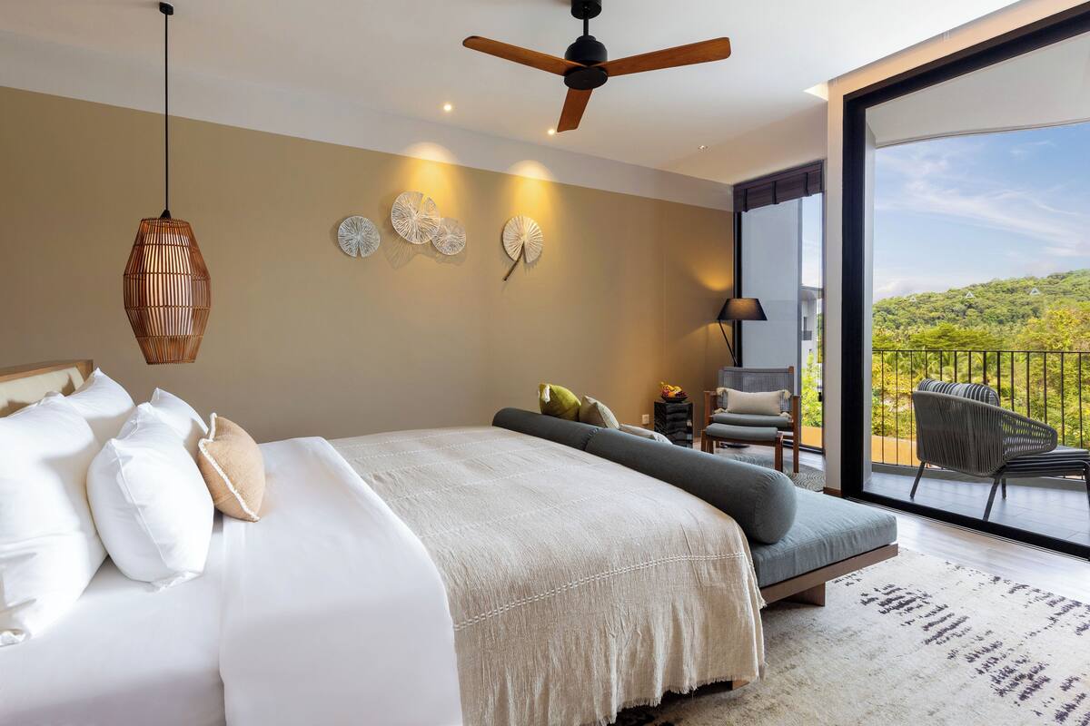 A bedroom with a large bed, a ceiling fan, and a balcony with a view of the hills.