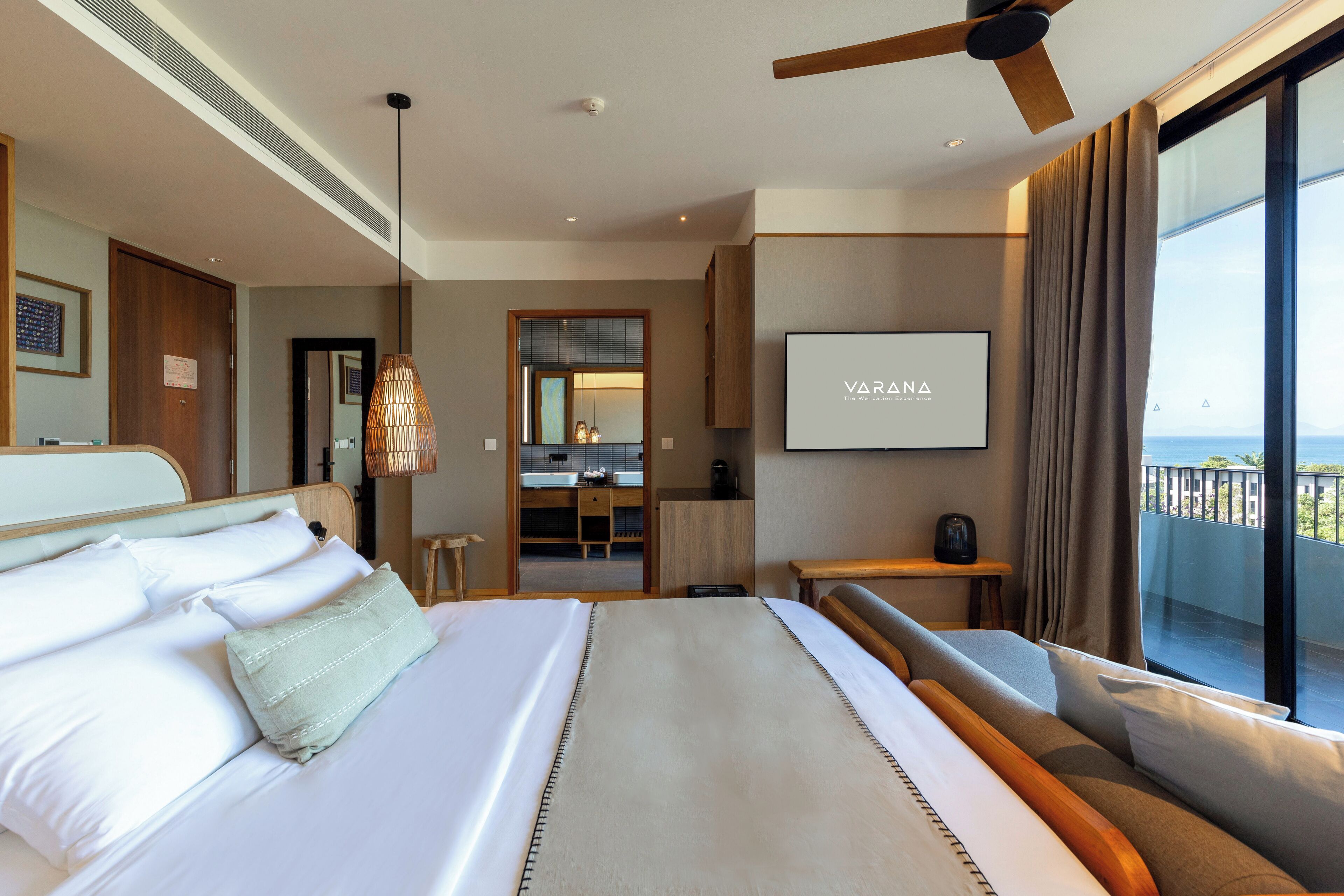 A hotel room with a large bed, a ceiling fan, a TV, and a balcony with a view.