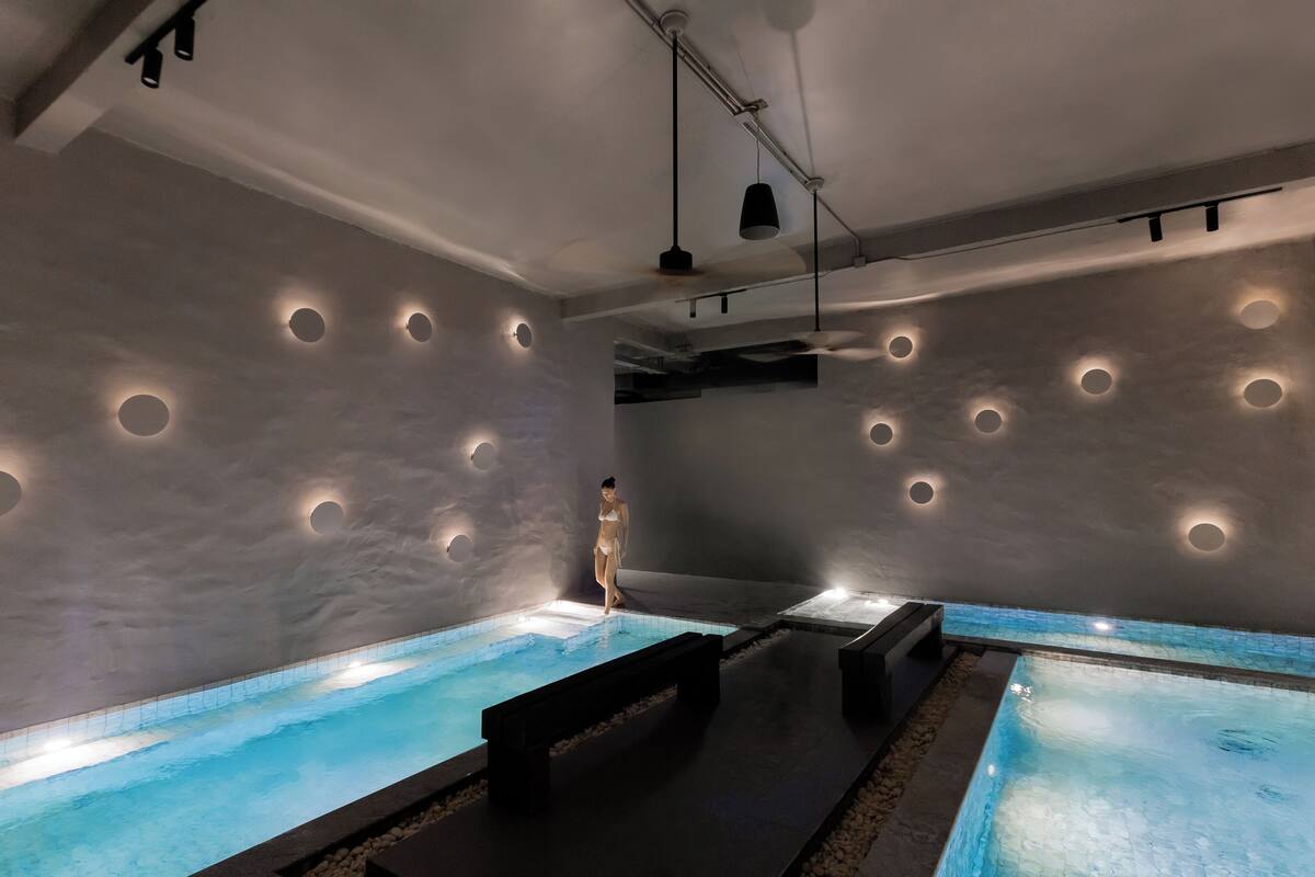 A spa area with two pools, a person in a swimsuit, and recessed lighting on the walls.