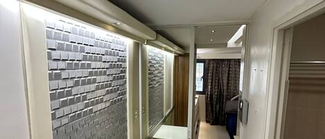 A corridor with a tiled wall, a white bench, and a door leading to another room.