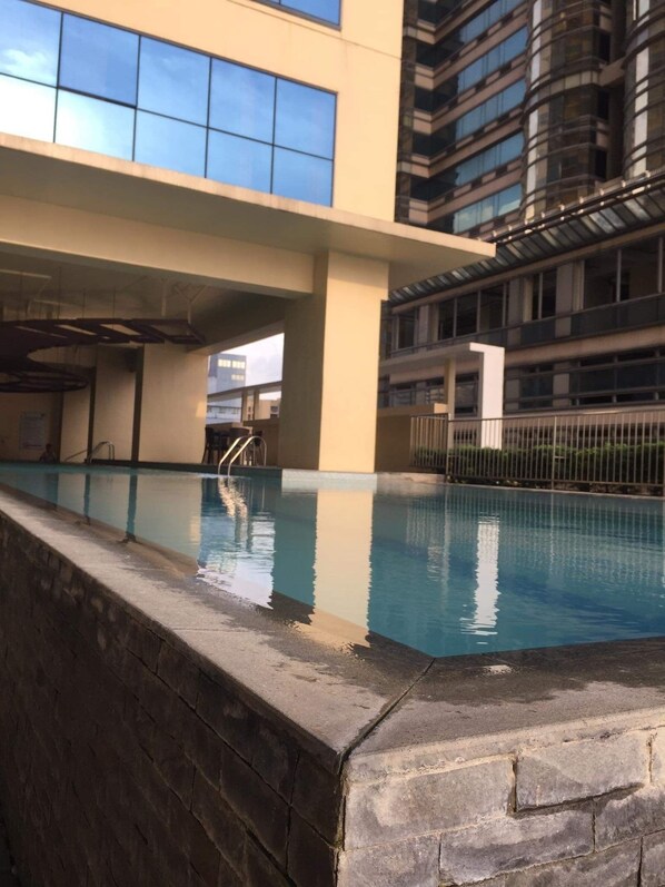 An indoor swimming pool with clear blue water, surrounded by a stone wall and a building with large windows in the background. - EMBASSYPOD 28  (Manila)