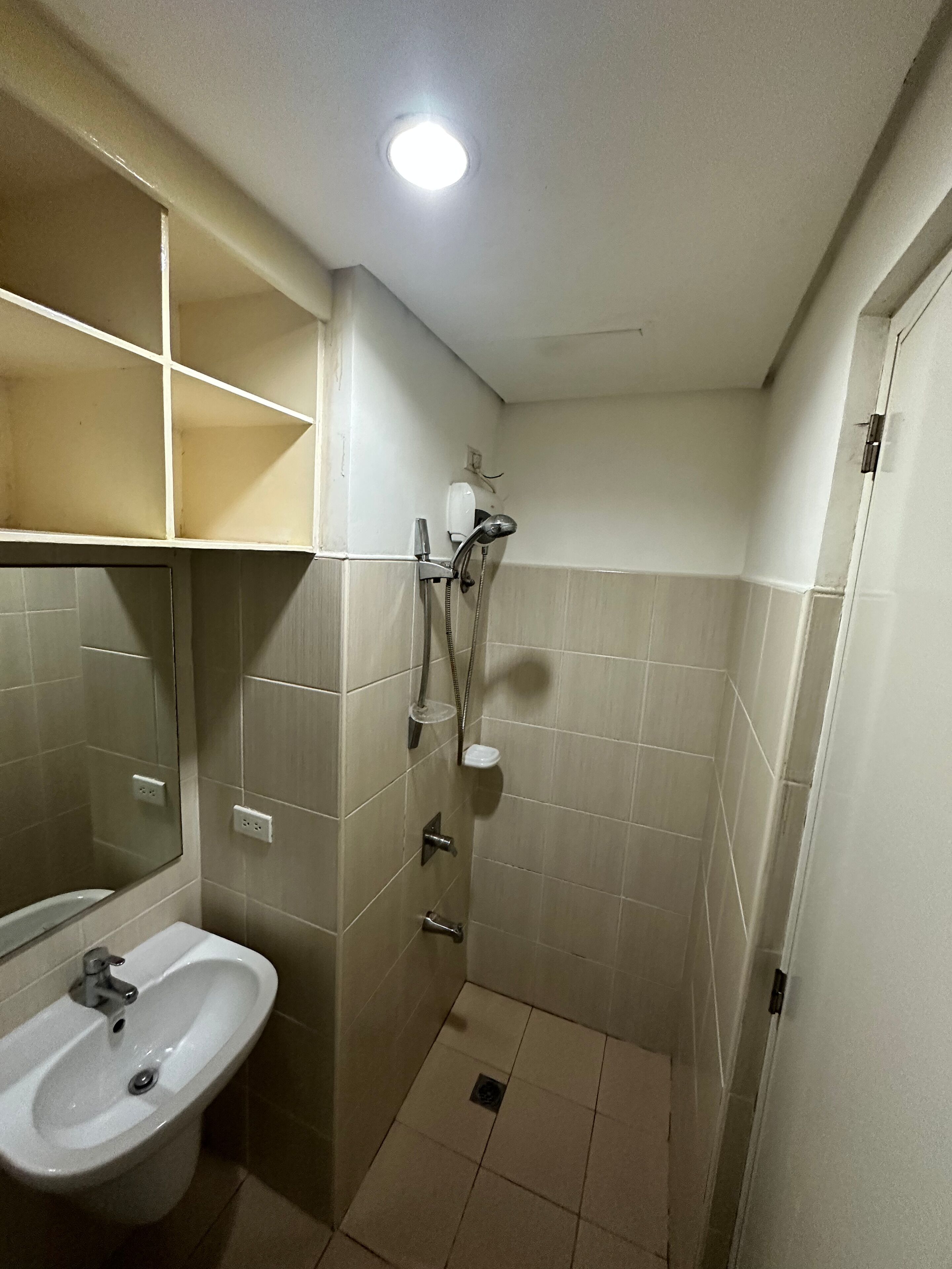 A small bathroom with a sink, mirror, shower, and tiled walls.