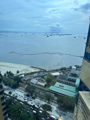A coastal cityscape with a view of the sea, buildings, and a road with vehicles. - EMBASSYPOD 28  (Manila)