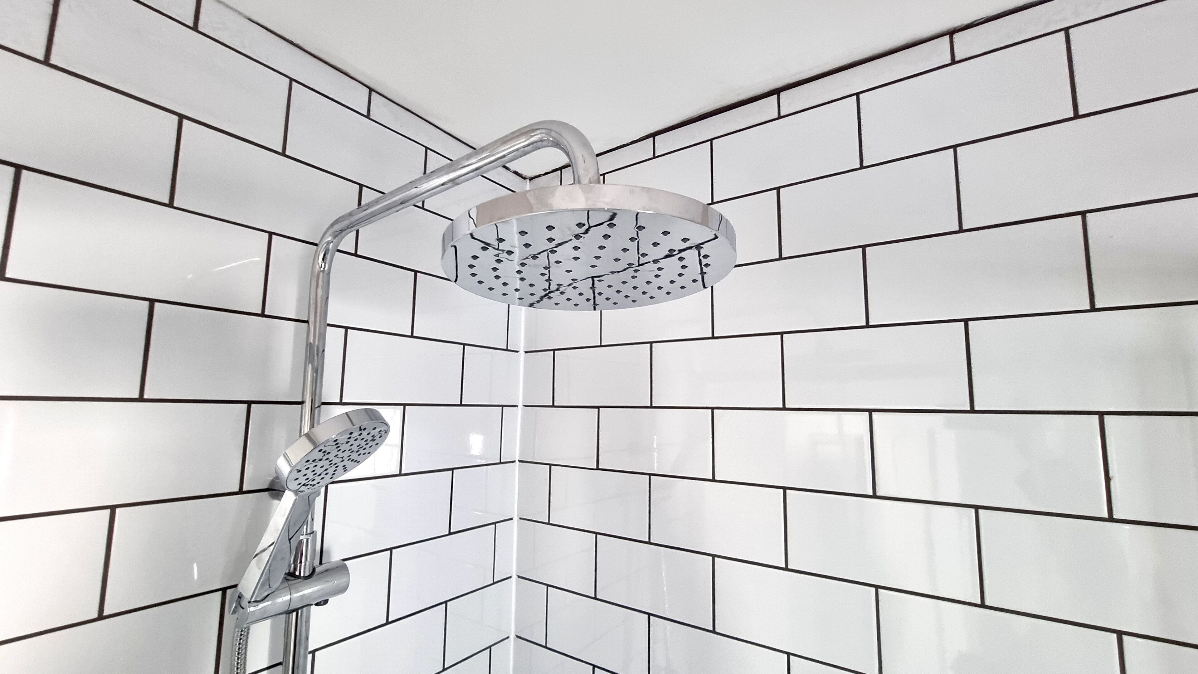 A shower with a rain showerhead and handheld showerhead, set against a white tiled wall with a herringbone pattern.