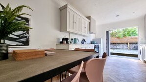 A modern kitchen with white cabinets, a dining table with chairs, a coffee machine, and a view of the outdoors. - Moorland House by Switchback Stays (Cardiff)