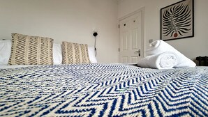 Una cama bien tendida con una colcha azul y blanca estampada, dos almohadas con diseño, una puerta blanca y una obra de arte enmarcada en la pared.
