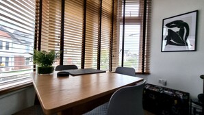 Un salón de conferencias con una mesa de madera, sillas, una planta en maceta y una obra de arte enmarcada en la pared.
