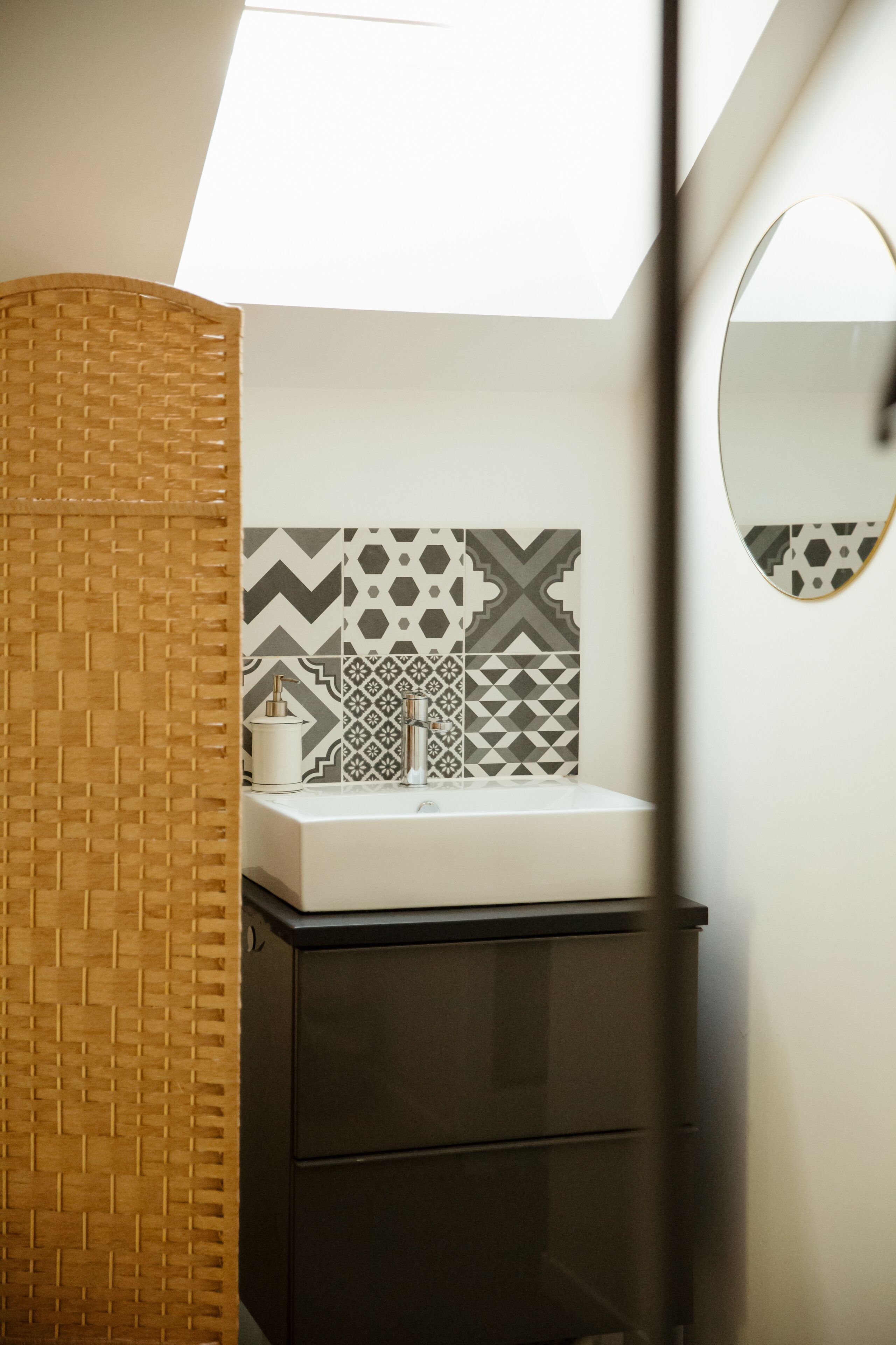 A bathroom with a white sink, patterned tiles, a wooden accent wall, and a mirror.