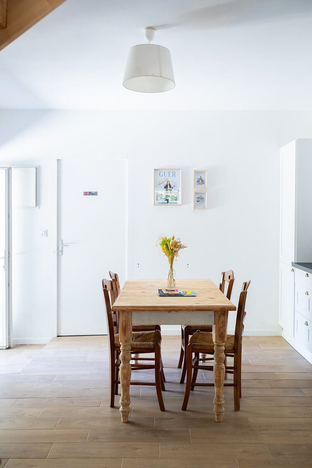 Un coin repas avec une table et des chaises en bois, un luminaire suspendu et des tableaux encadrés au mur.
