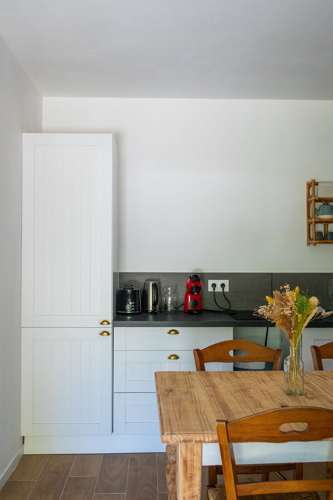A compact kitchen with white cabinetry, a wooden dining table, and a coffee maker on the counter.