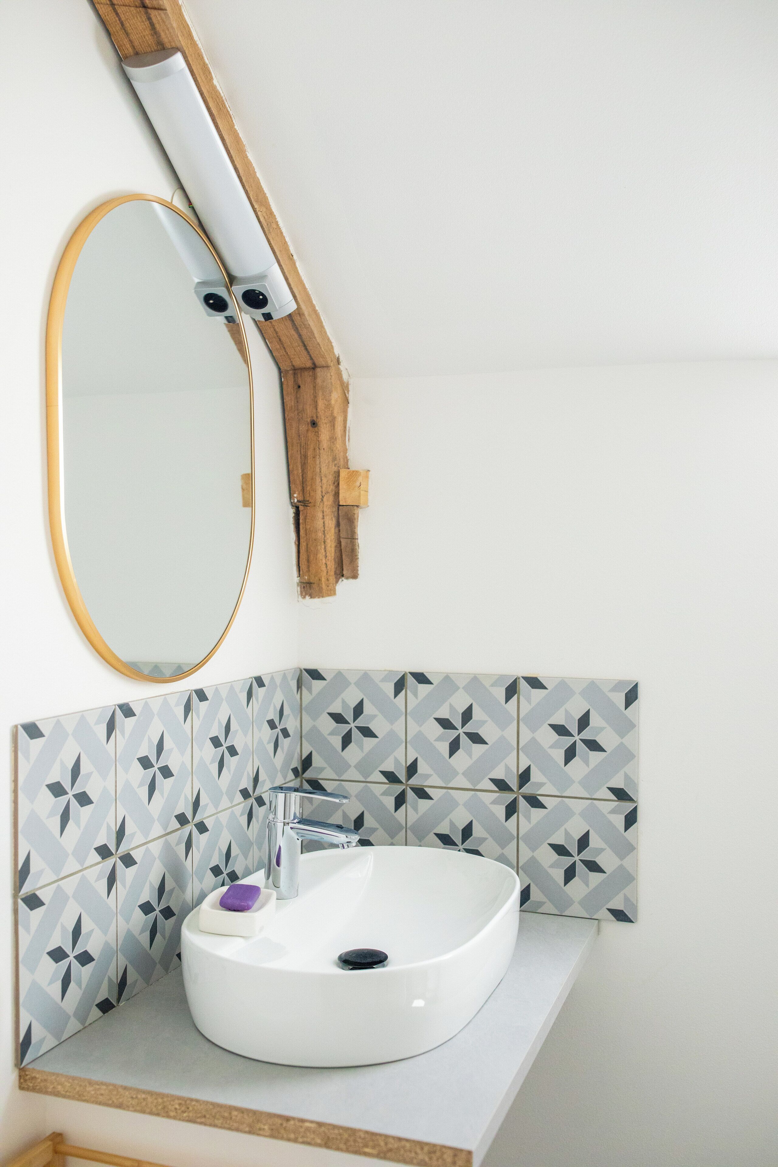 Un baño con lavamanos blanco, un espejo y baldosas con diseño geométrico.
