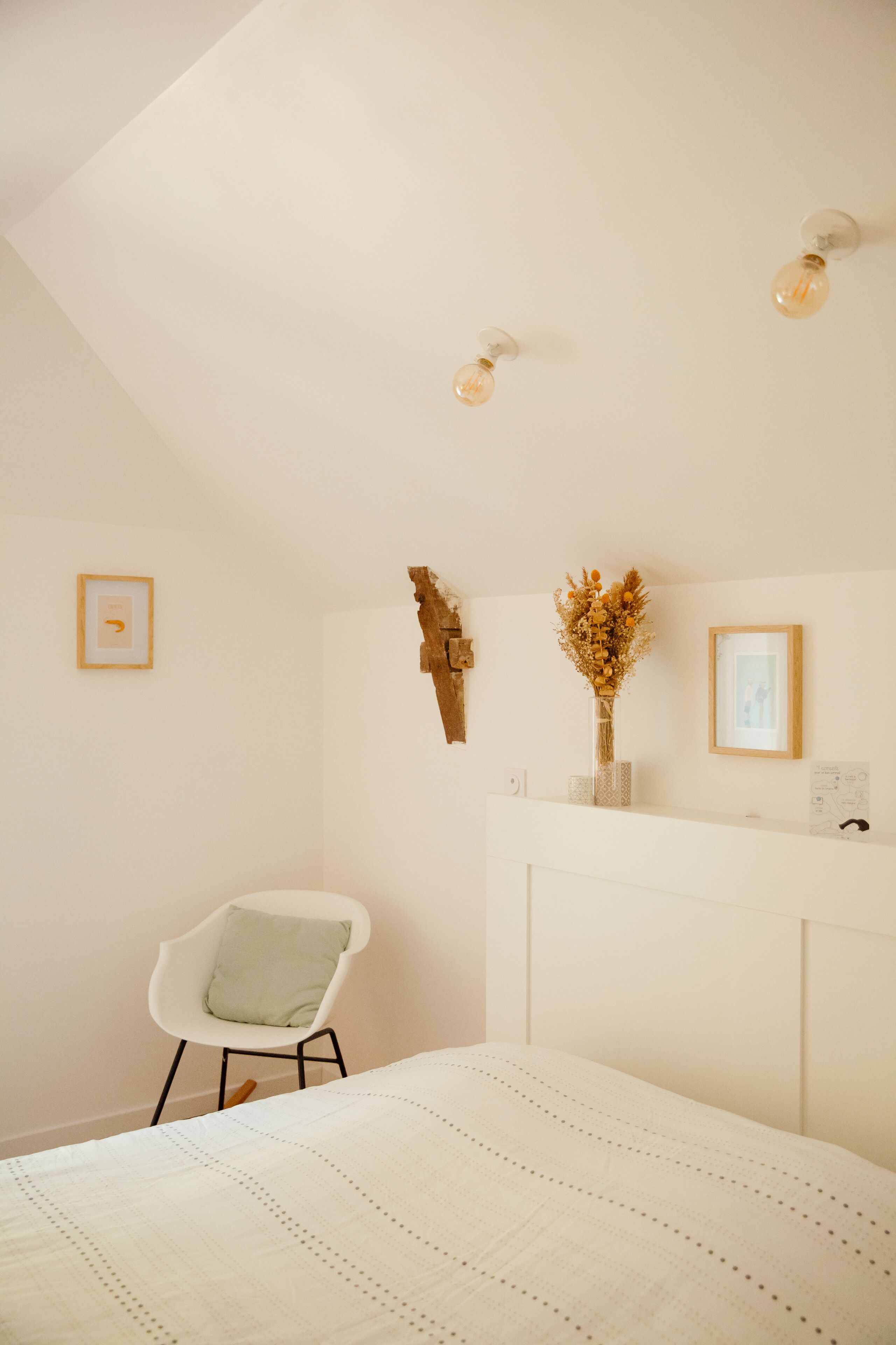 Un dormitorio con cama, una silla, un escritorio e iluminación en la pared.