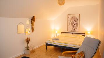 Een slaapkamer met een bed, bedlampen, een stoel, een kunstwerk aan de muur en een kleine potplant.