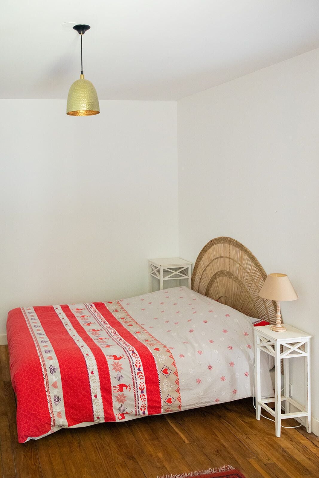Een slaapkamer met een bed, een bedlampje, een klein wit nachtkastje en een hangende lamp.