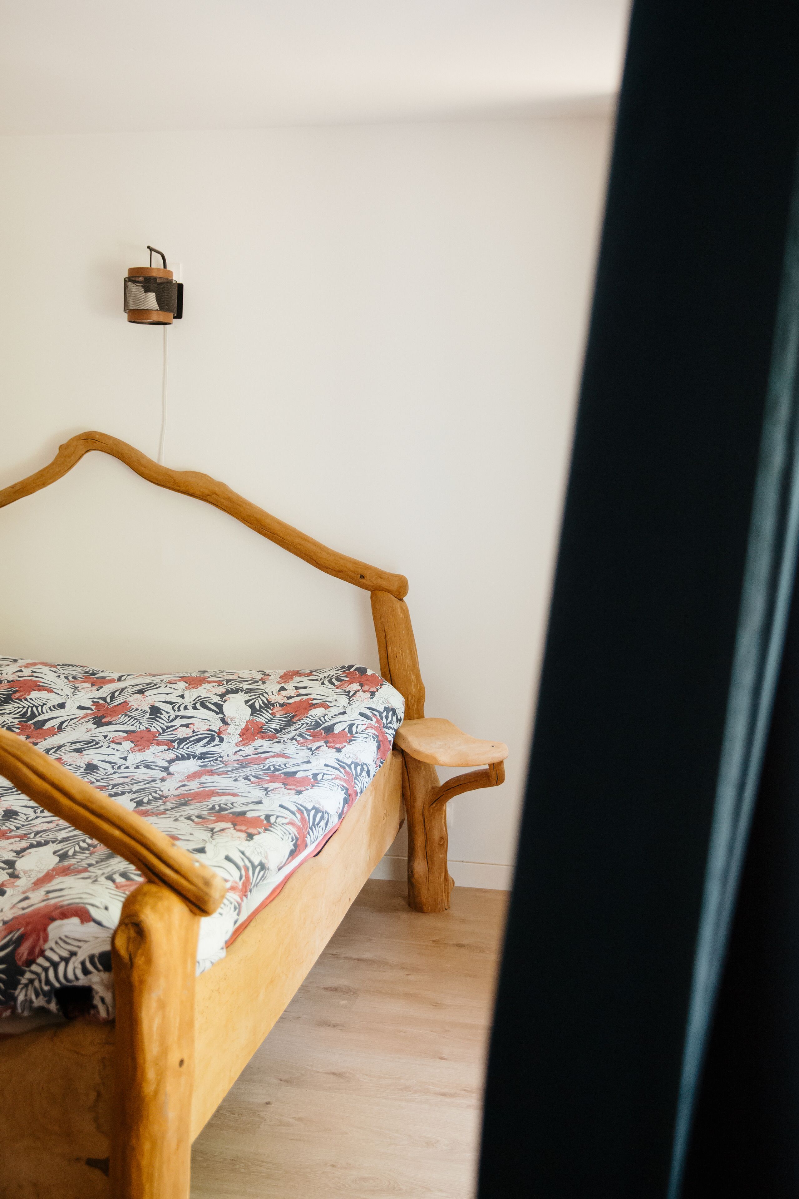 A wooden bed with a patterned bedspread in a room with a white wall and a small bedside table.