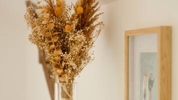 A clear vase with dried flowers and ribbons on a white shelf, next to a framed picture and patterned boxes.