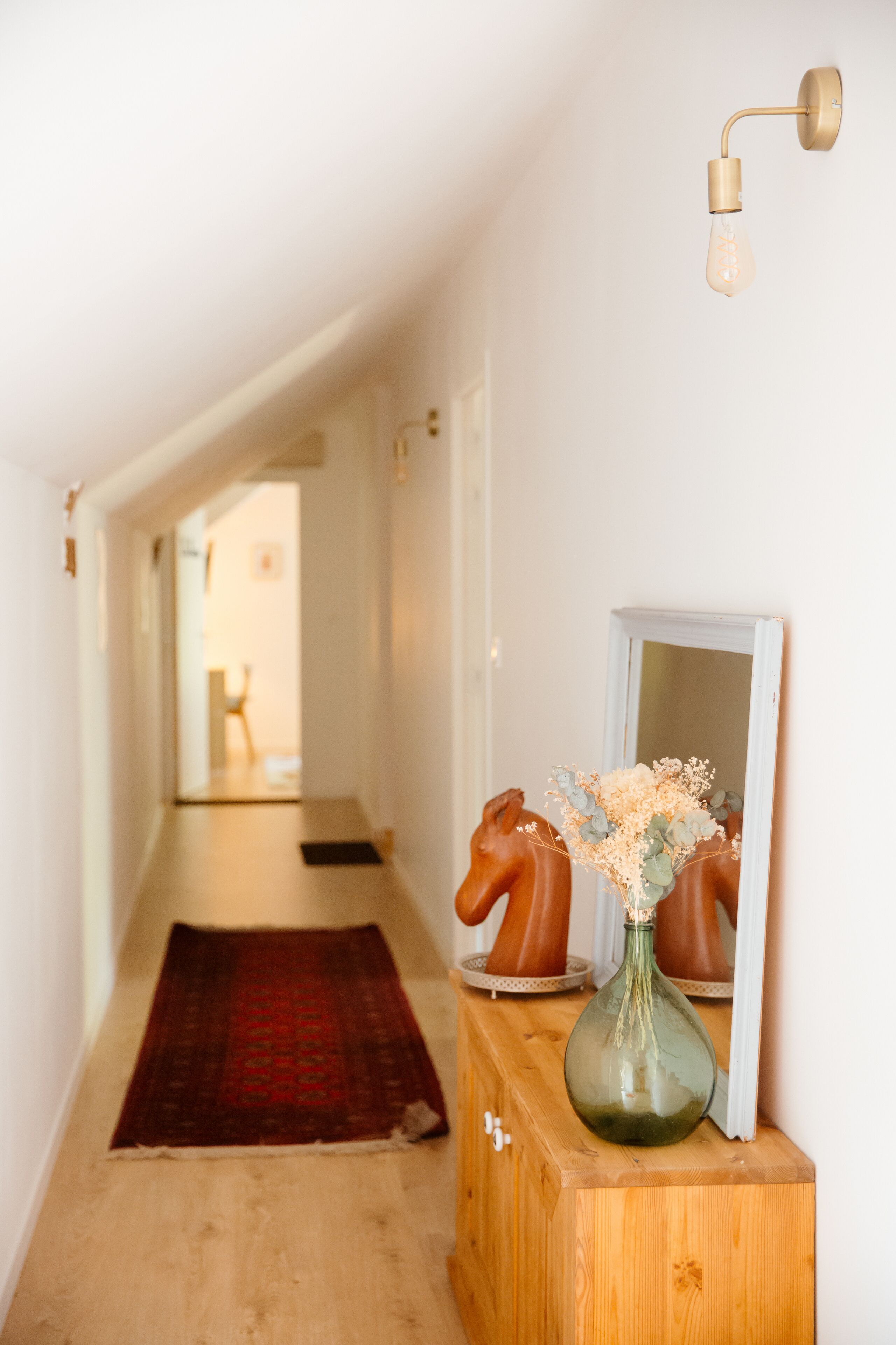 A hallway with a wooden cabinet, a mirror, and a vase with flowers.