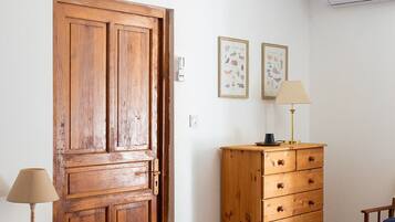 Una stanza con una porta in legno, un comò, una lampada, una sedia e un letto con copriletto a motivi rossi e bianchi.