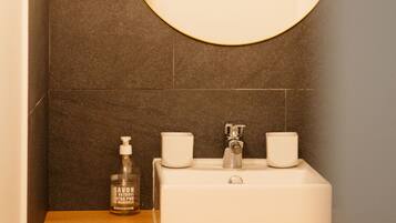 A bathroom with a round mirror, a white sink, a soap dispenser, and a cup.