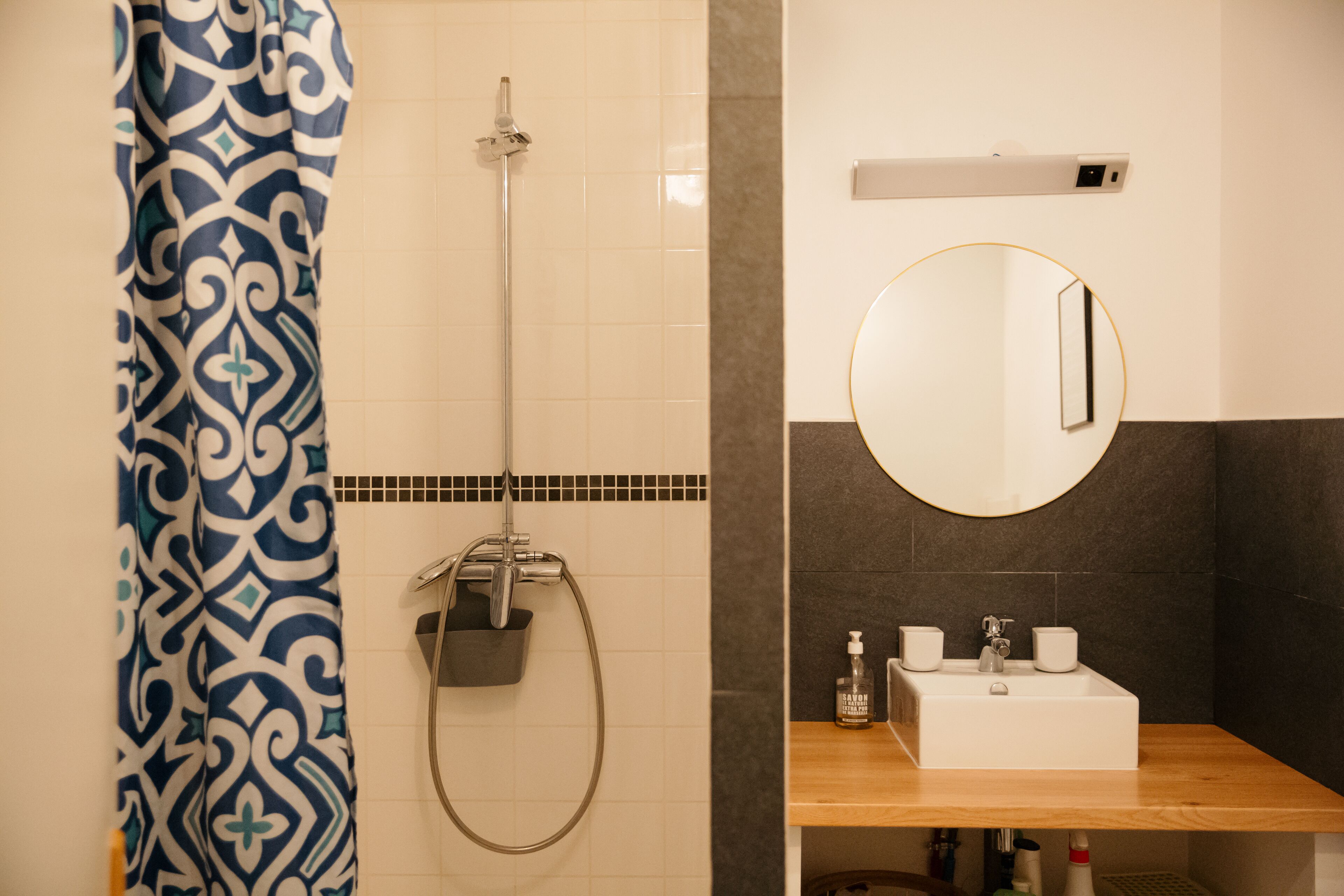 A bathroom with a shower, a sink with a mirror, and a patterned shower curtain.