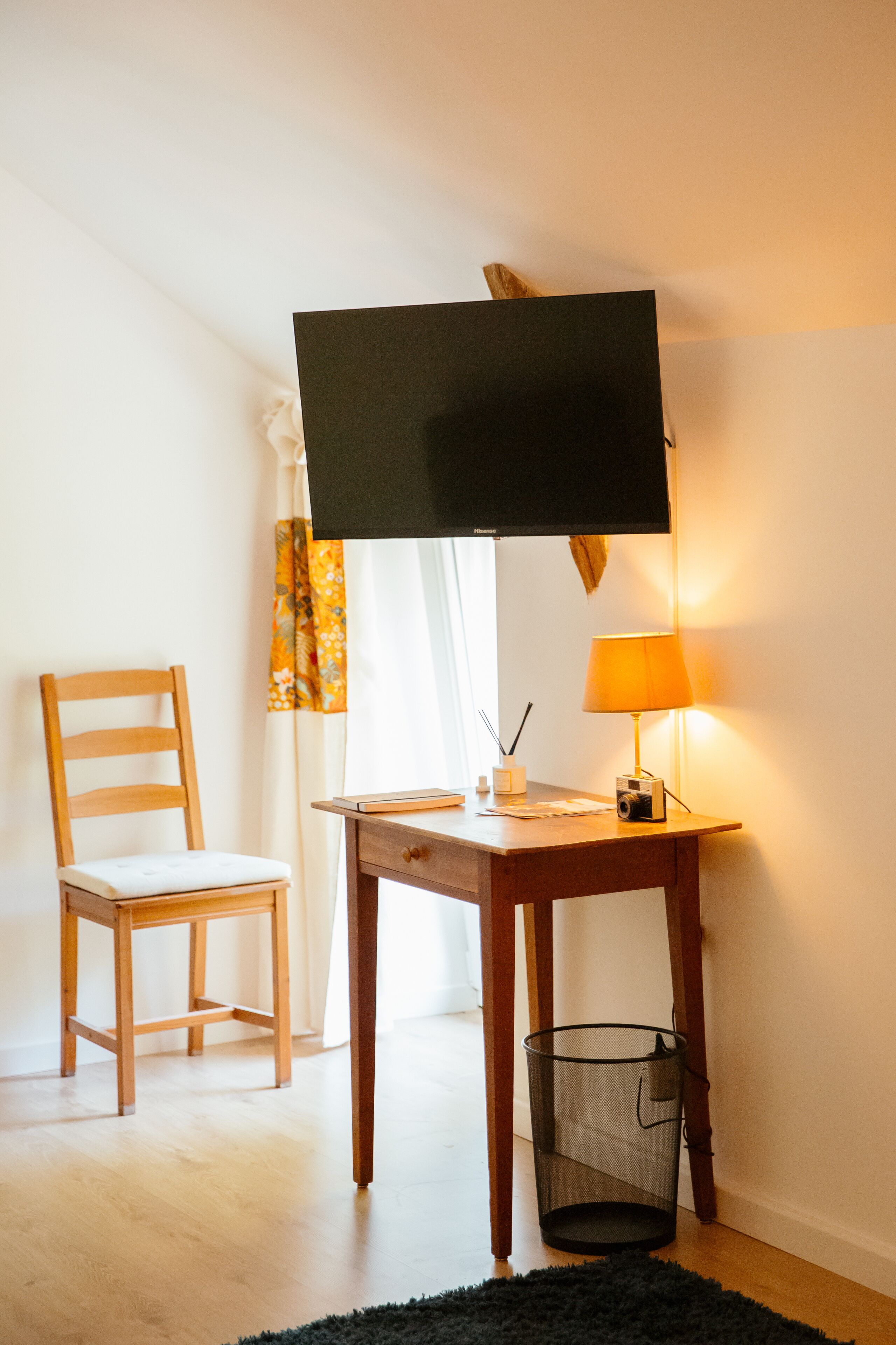 A room with a desk, chair, television, lamp, and waste basket.