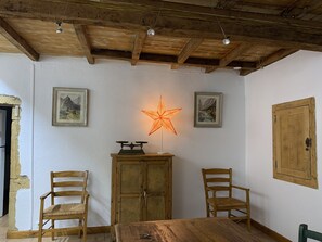 A rustic room with wooden beams, a wooden table, two chairs, a cabinet, and two framed pictures on the wall.