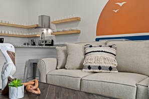 Moderni olohuone, jossa on harmaa sohva, koristeellinen tyyny, puuveistos ja pieni kasvi.