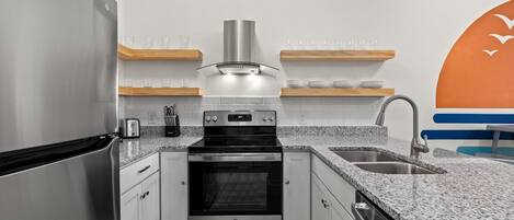A modern kitchen with stainless steel appliances, granite countertops, and wooden shelves.