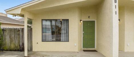 Una casa de un piso con una puerta verde, una ventana con cortinas y un buzón.
