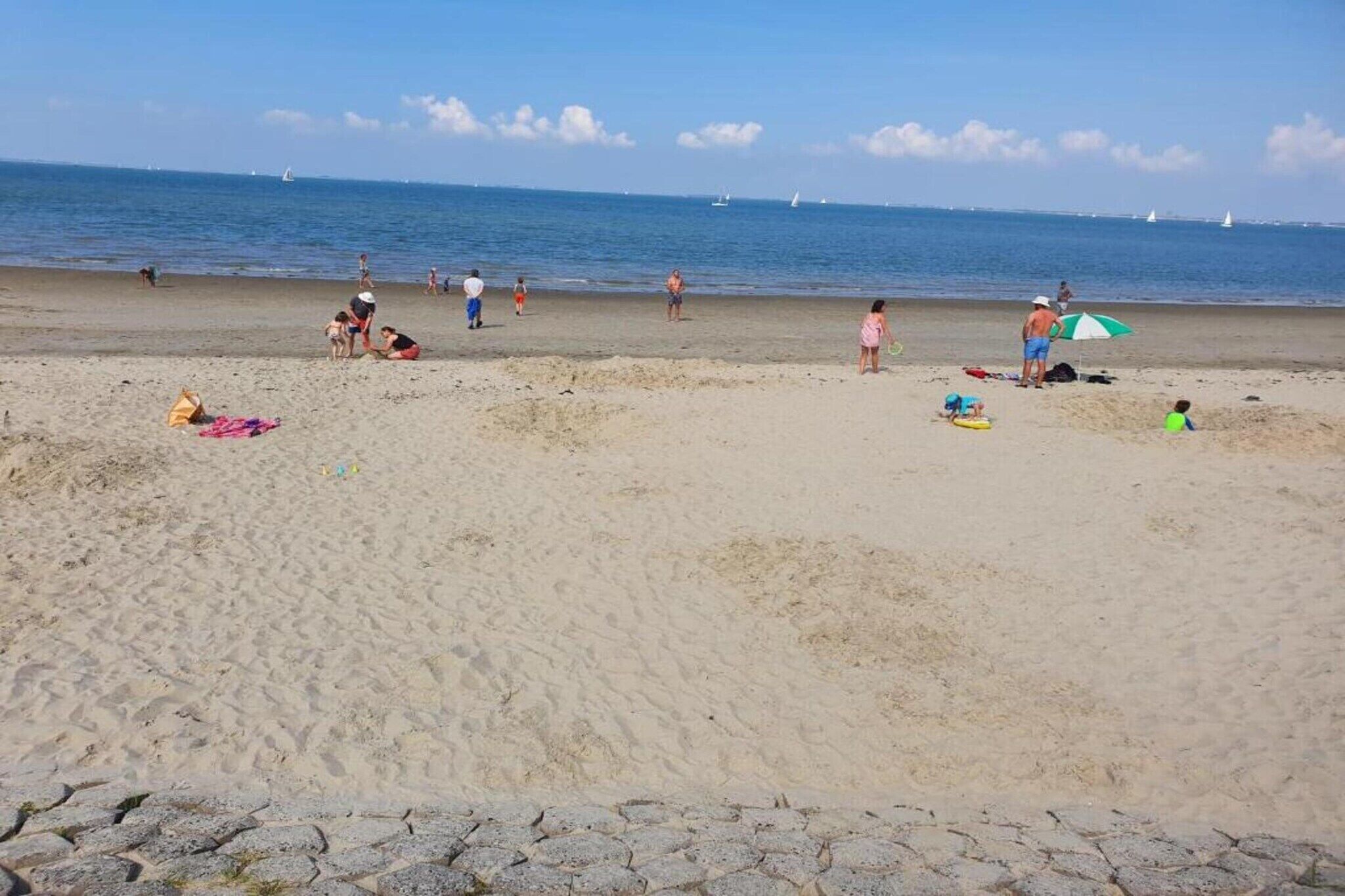 Una playa arenosa con gente y barcos al fondo.