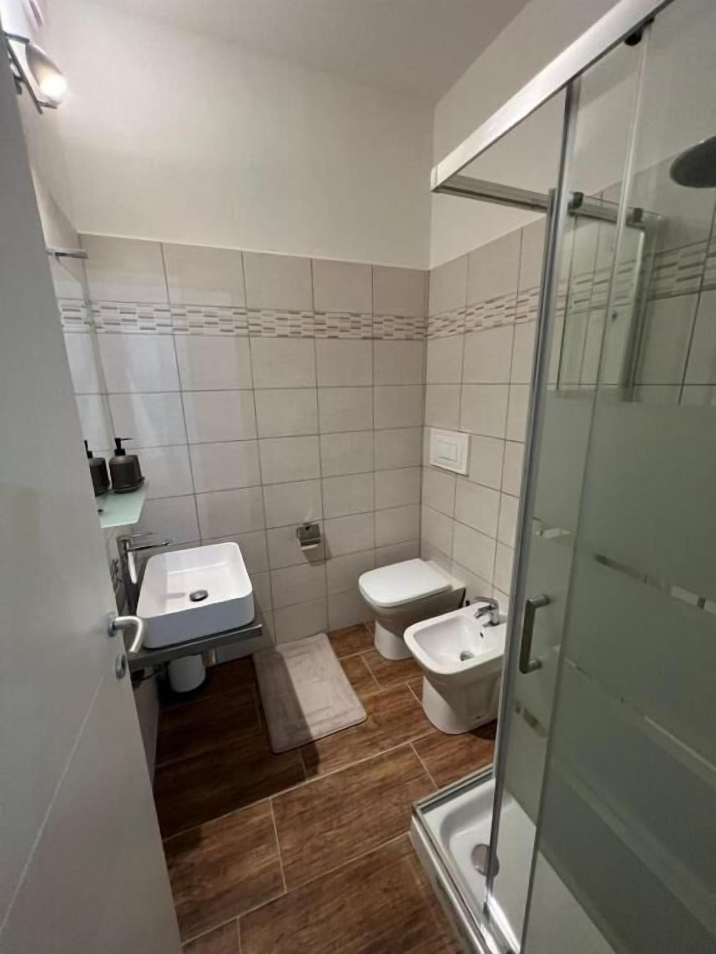 Un bany modern amb un espai de dutxa de vidre, un lavabo blanc, un vàter i un bidet.