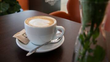Una taza de café sobre un plato, una cuchara, una tarjeta pequeña y un florero con flores sobre una mesa.