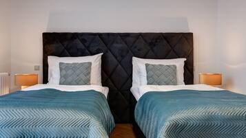 A double bed with a tufted headboard, two pillows, and matching blue bedspreads.