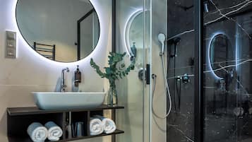 Een moderne badkamer met een glazen douchecabine, een ronde spiegel en een witte wastafel.